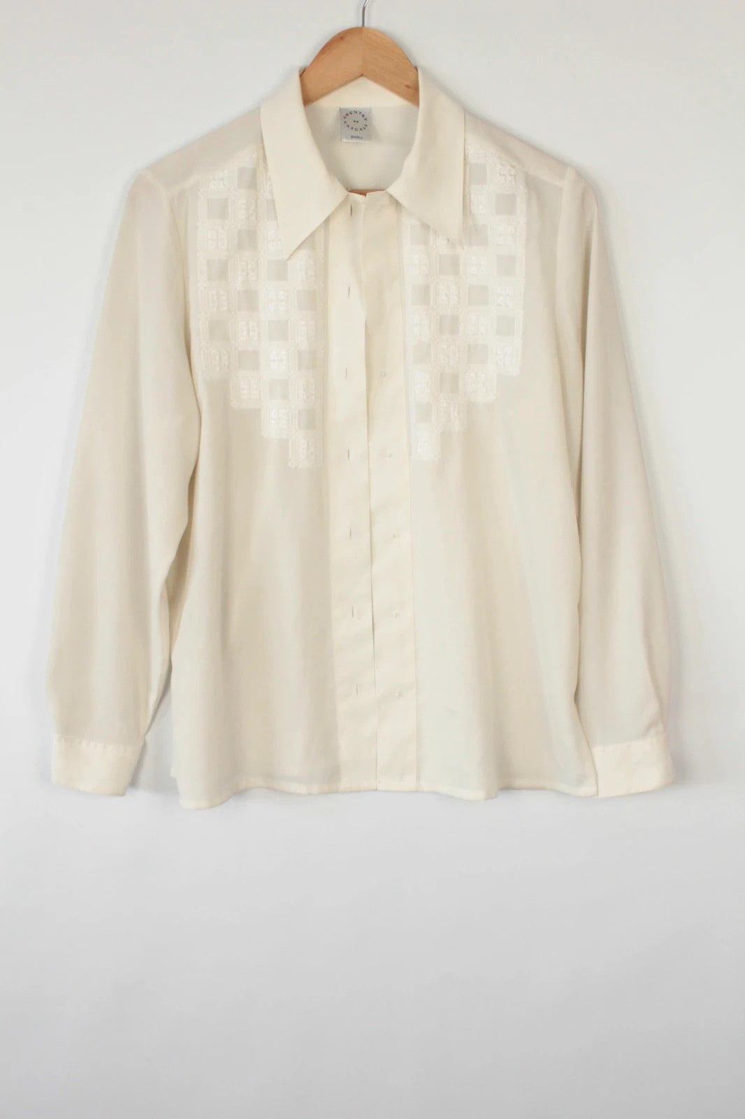 Country Casuals cream tunic blouse with embroidered checkerboard bib and long sleeves.