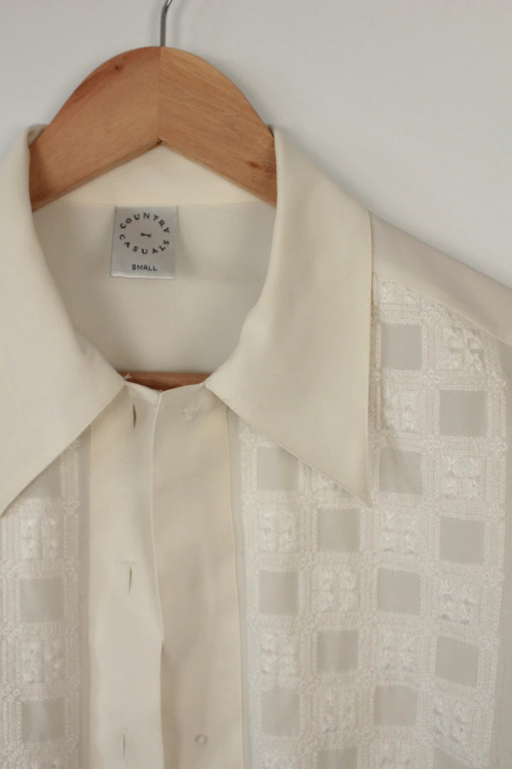 Country Casuals cream tunic blouse with embroidered checkerboard bib and long sleeves.