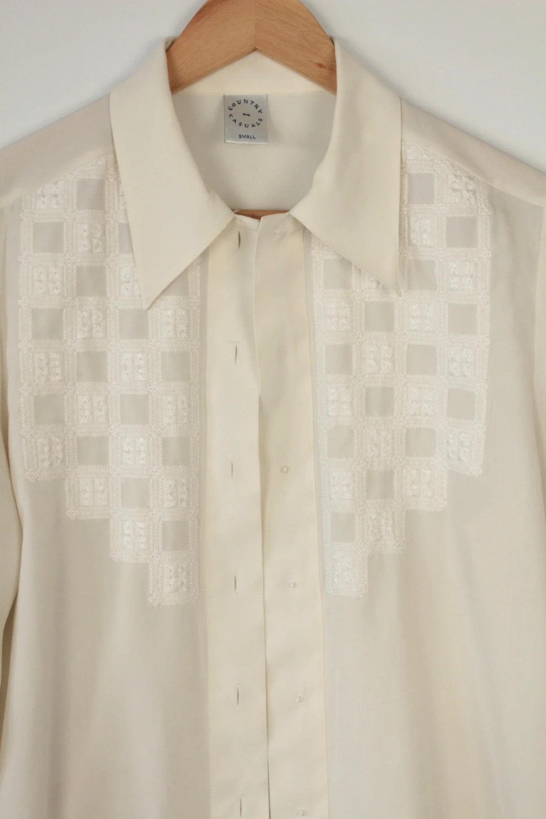 Country Casuals cream tunic blouse with embroidered checkerboard bib and long sleeves.