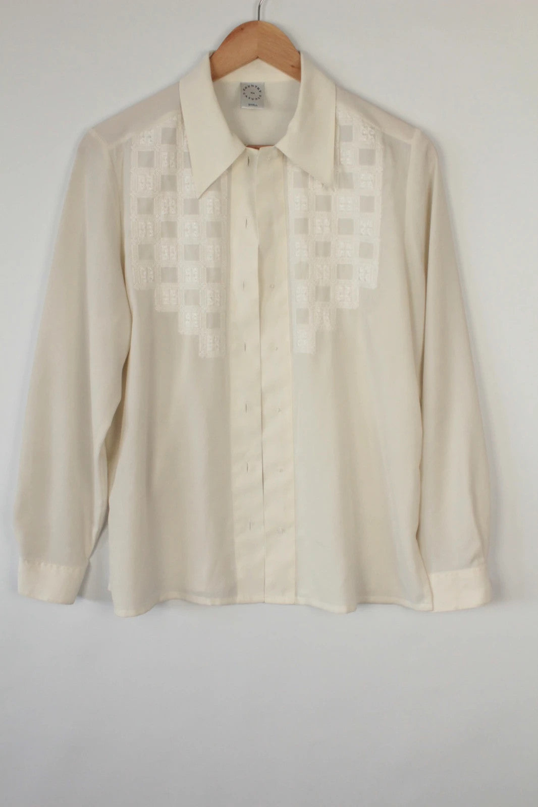 Country Casuals cream tunic blouse with embroidered checkerboard bib and long sleeves.