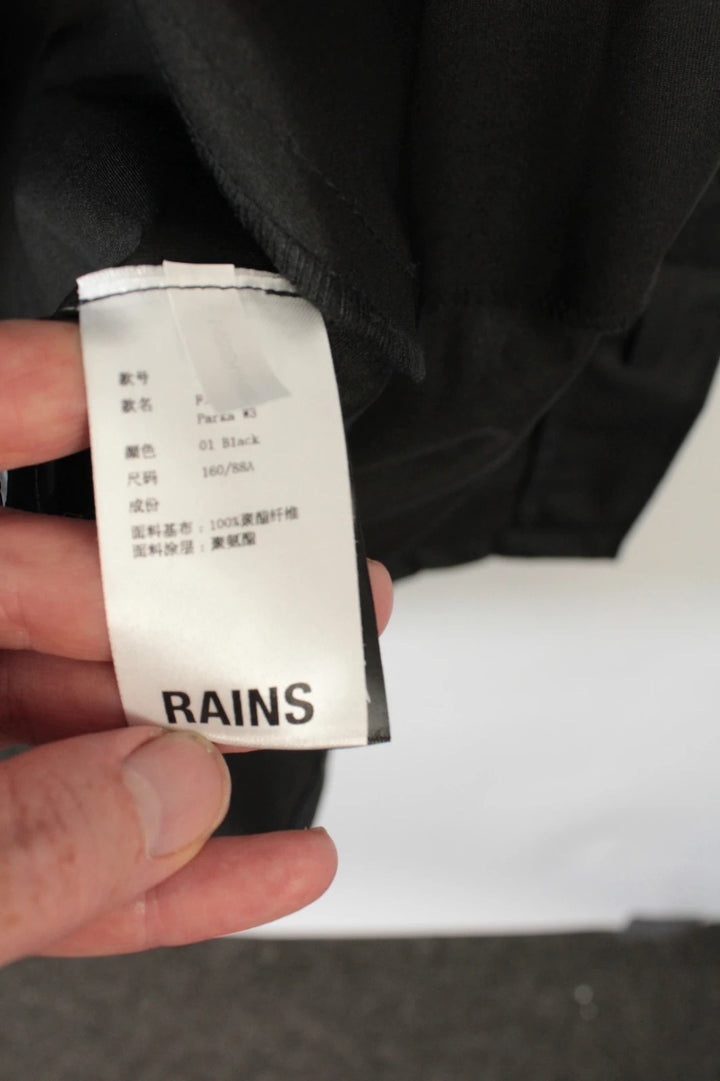 Rains black fishtail parka jacket with adjustable hood and matte finish.