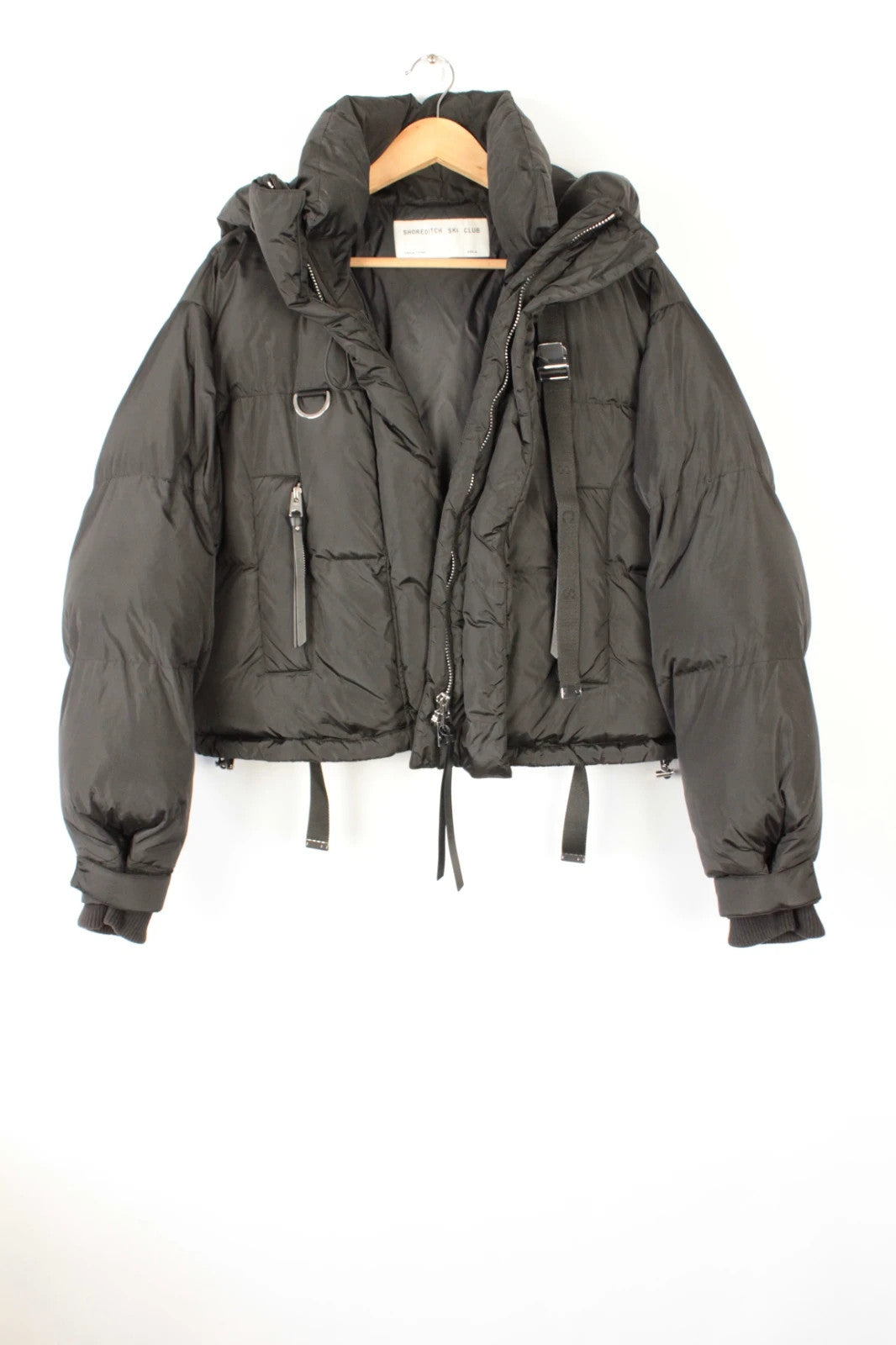 Shoreditch Ski Club black cropped puffer jacket with quilted matte shell and harness straps.