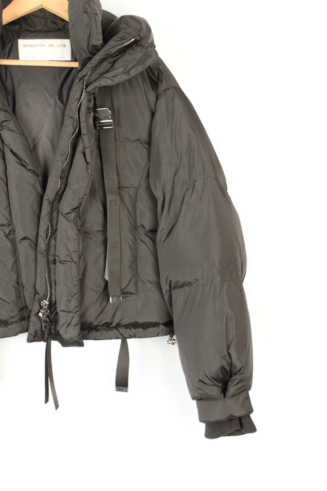 Shoreditch Ski Club black cropped puffer jacket with quilted matte shell and harness straps.