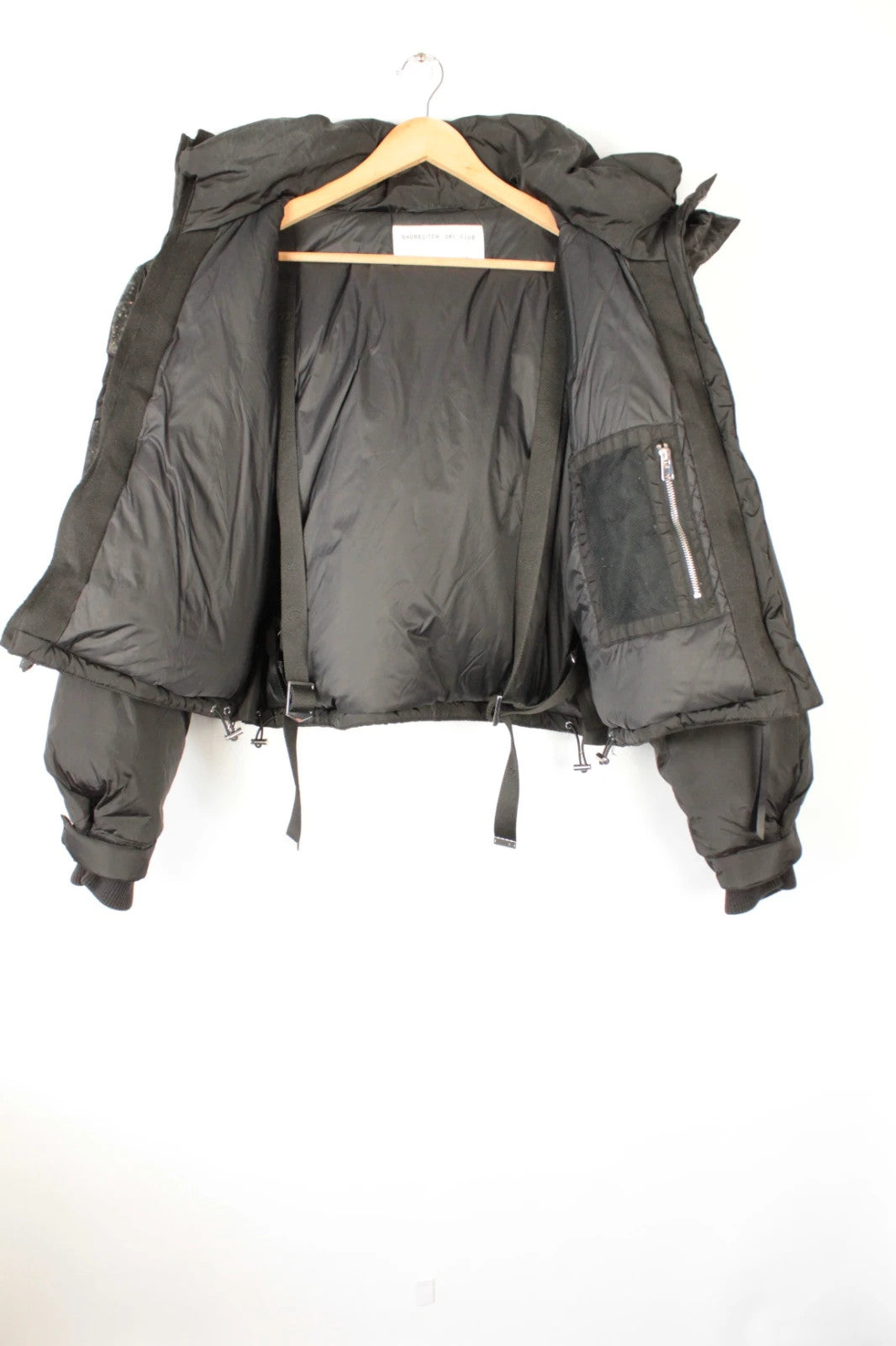 Shoreditch Ski Club black cropped puffer jacket with quilted matte shell and harness straps.