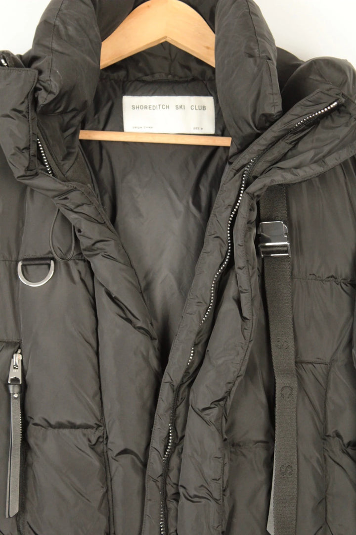 Shoreditch Ski Club black cropped puffer jacket with quilted matte shell and harness straps.