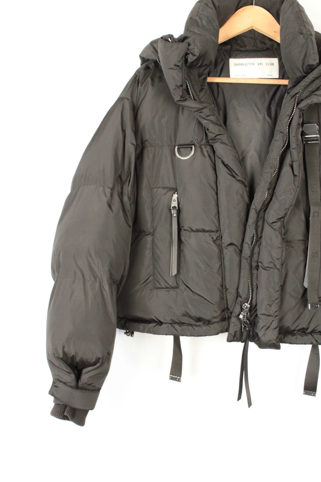 Shoreditch Ski Club black cropped puffer jacket with quilted matte shell and harness straps.