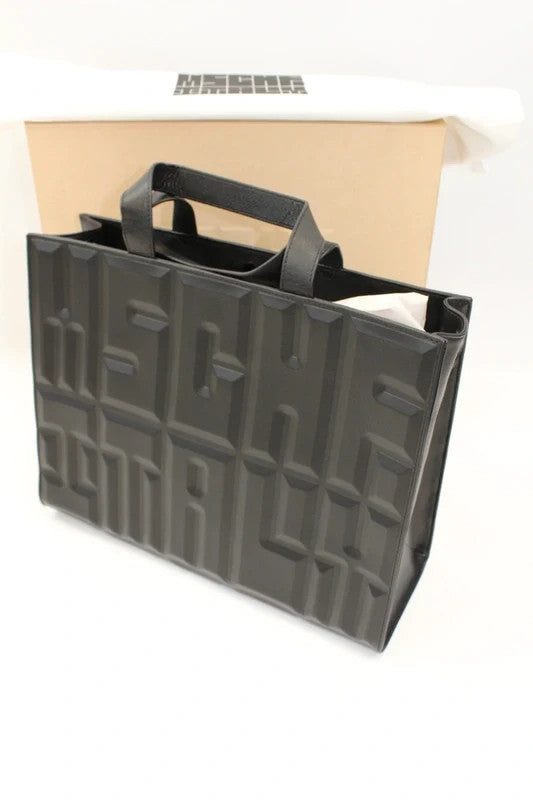 MSCHF black leather tote bag with embossed geometric lettering and dual top handles.