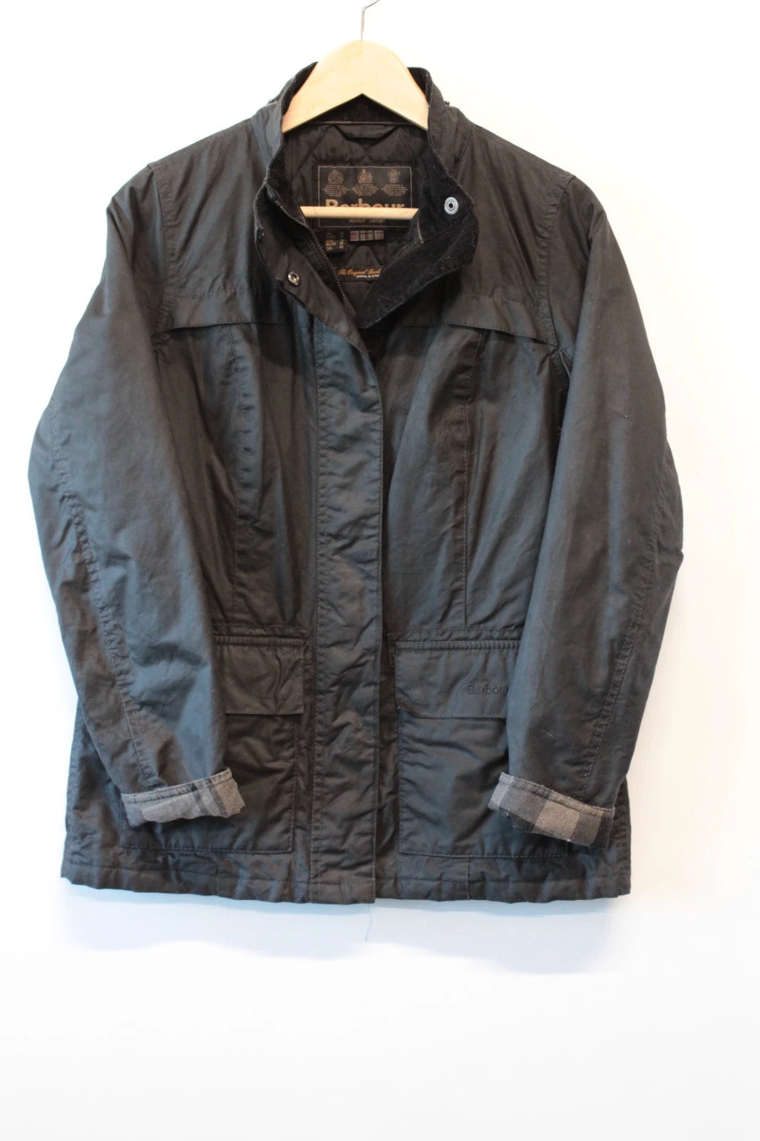 Barbour black waxed cotton jacket with tartan pattern and corduroy collar accent.