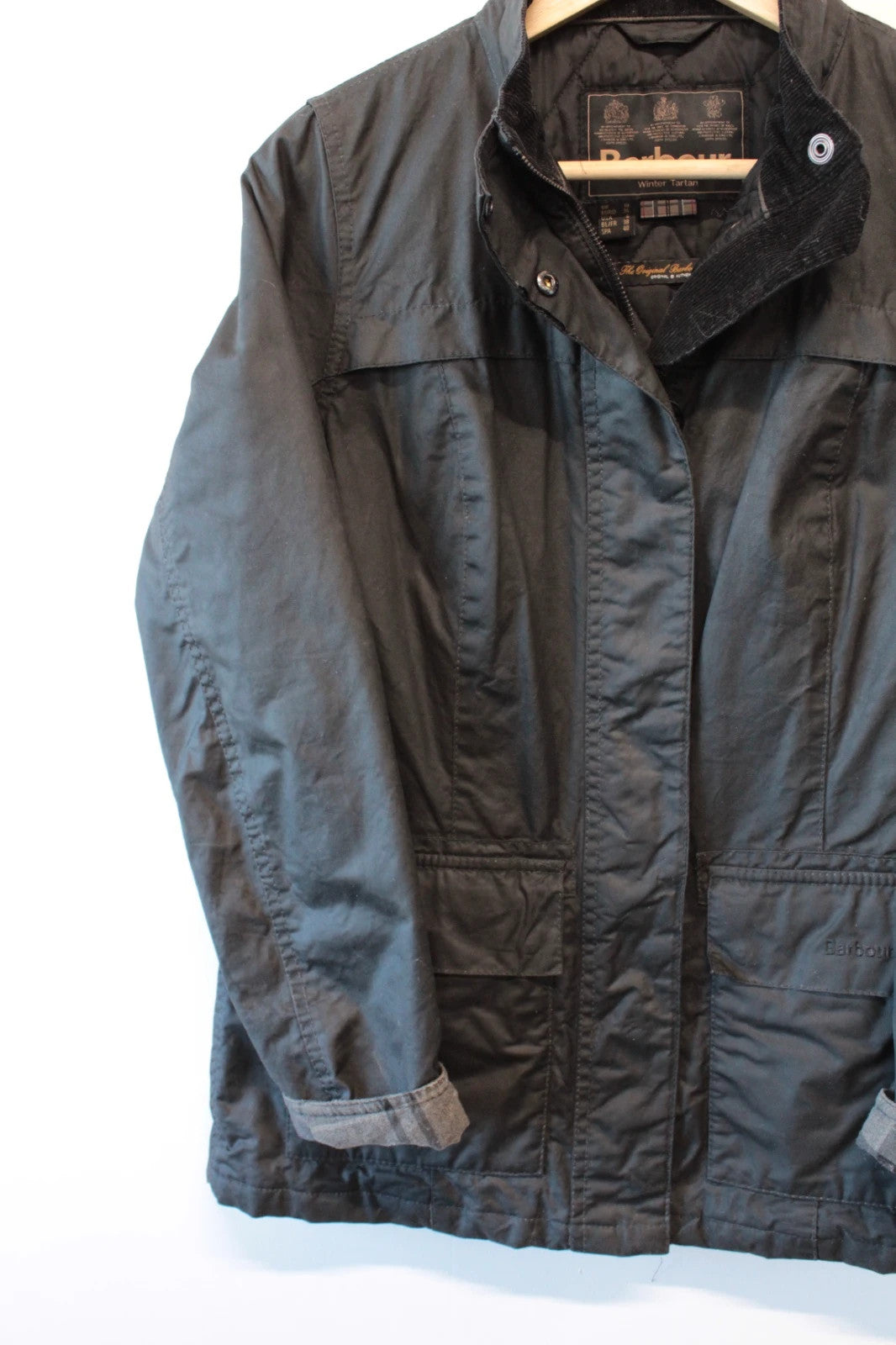 Barbour black waxed cotton jacket with tartan pattern and corduroy collar accent.