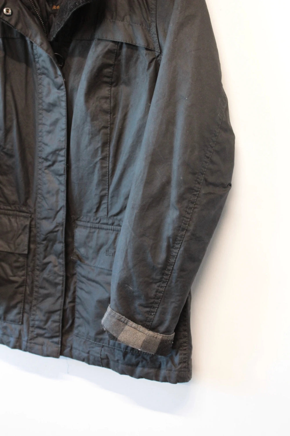 Barbour black waxed cotton jacket with tartan pattern and corduroy collar accent.