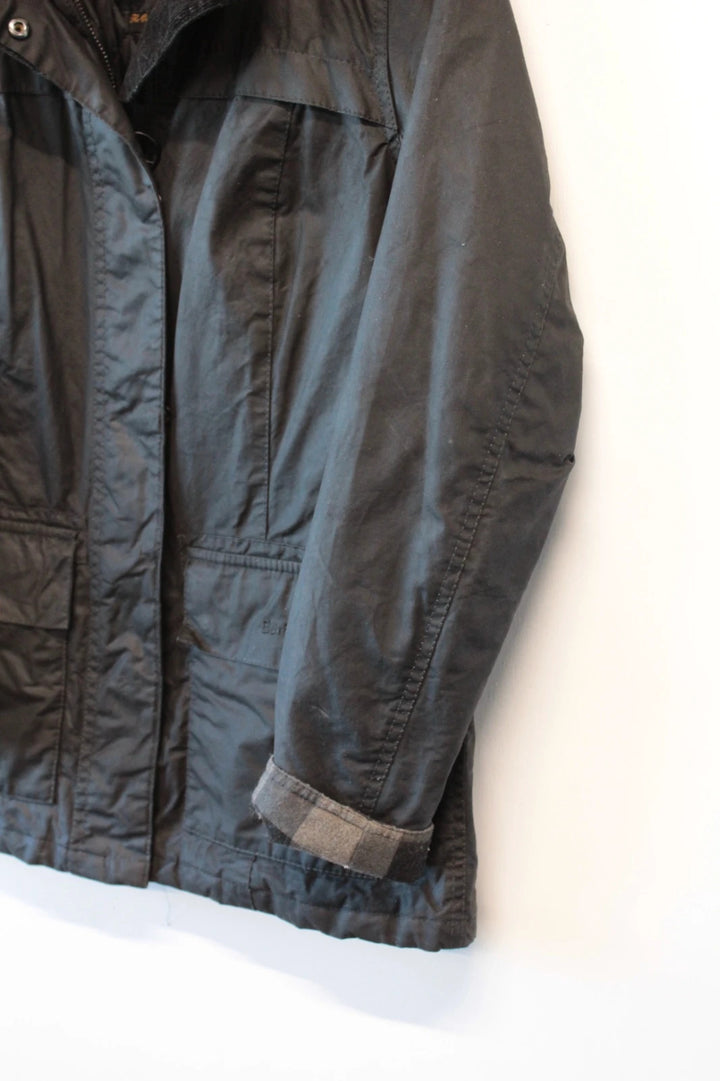 Barbour black waxed cotton jacket with tartan pattern and corduroy collar accent.