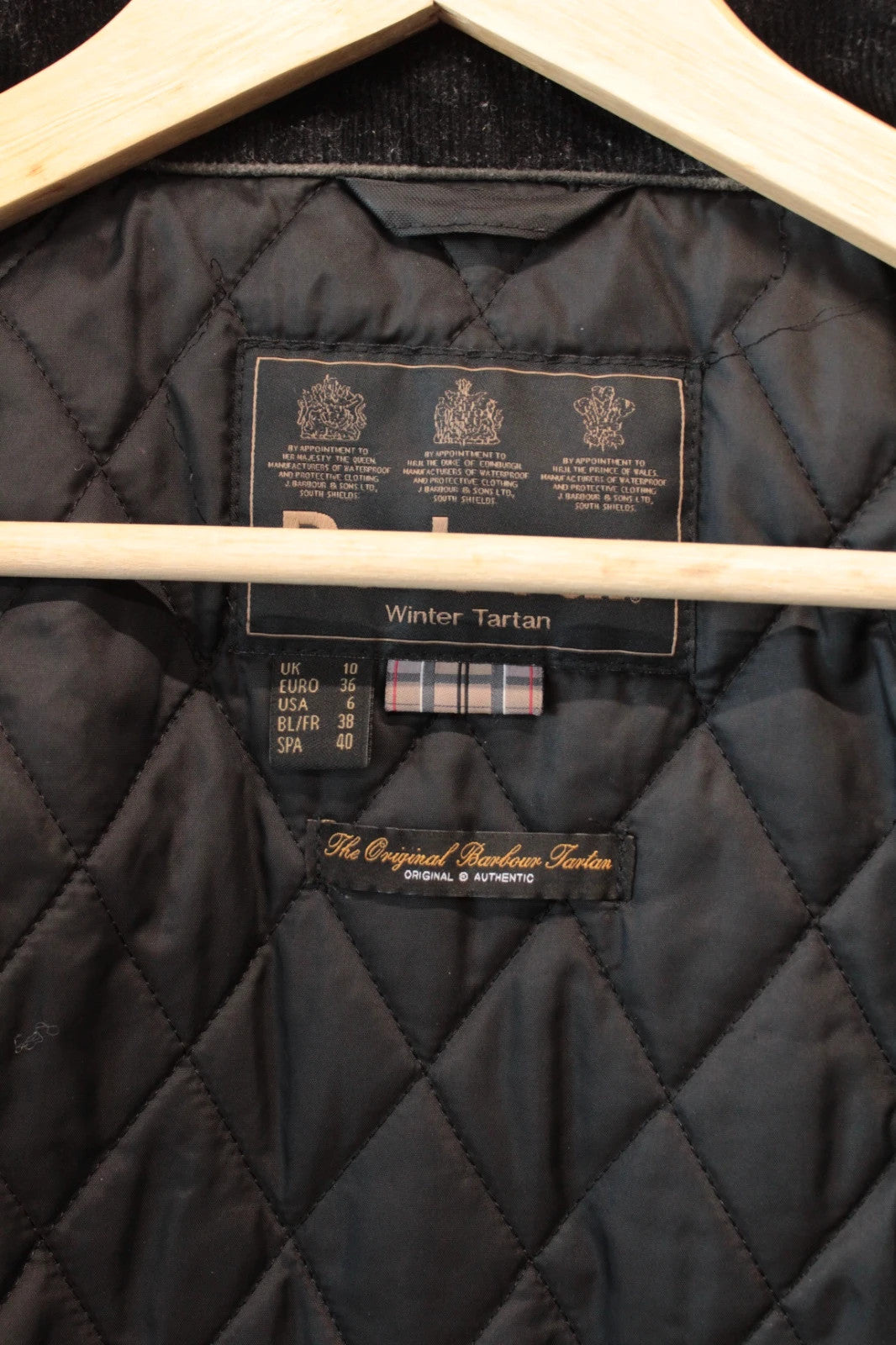 Barbour black waxed cotton jacket with tartan pattern and corduroy collar accent.