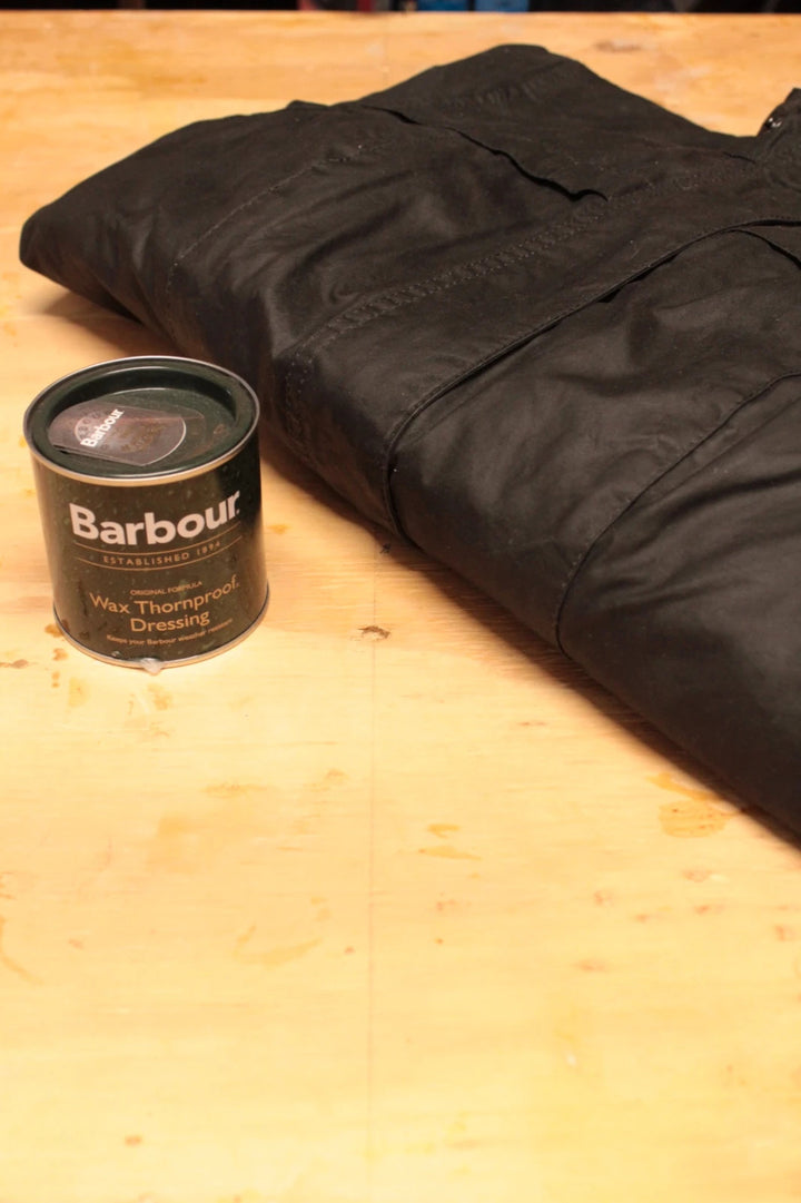Barbour black waxed cotton jacket with tartan pattern and corduroy collar accent.