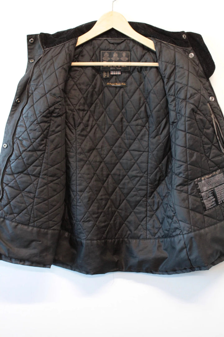Barbour black waxed cotton jacket with tartan pattern and corduroy collar accent.